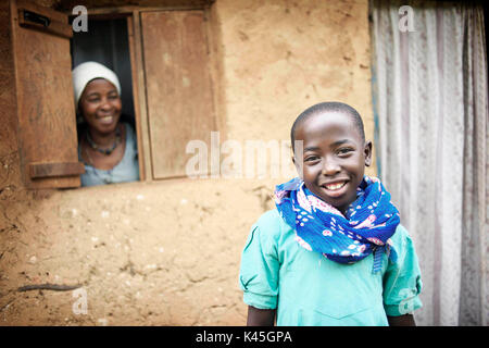 Portrait d'une jeune Ougandaise à la maison avec sa mère, pendant qu'elle regarde fixement à travers une fenêtre à leur maison rurale Banque D'Images