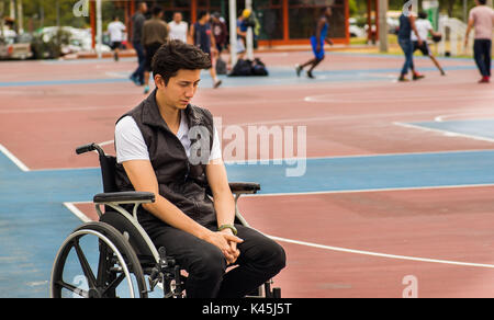 Triste bel homme dans un fauteuil roulant pendant à pied dans le parc, à la façon dont d'autres personnes font du sport, le soccer et le basket-ball, à Quito Banque D'Images