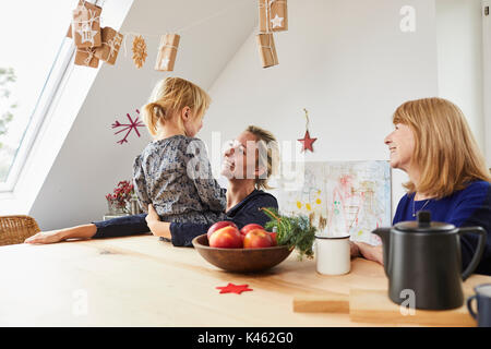 Grand-mère, mère et petite fille avec calendrier de l'Avent, assis à la table de la cuisine, Banque D'Images