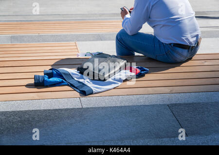 L'homme est assis sur un banc et utilise un téléphone mobile. Banque D'Images