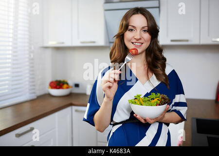 Happy pregnant woman standing dans la cuisine manger la salade. Banque D'Images
