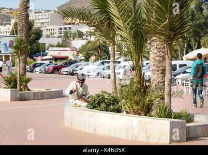 Agadir. Maroc - le 23 décembre 2016 : l'homme marocain de manger des aliments sur la promenade de bord de plage à Agadir Banque D'Images