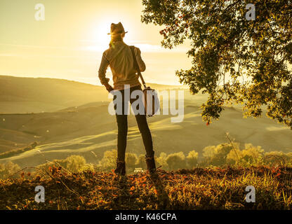 Découvrir une vue magique de la Toscane. Vu de dos active woman in hat avec sac Randonneur admirant le coucher du soleil en Toscane Banque D'Images