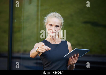 Face portrait of confident businesswoman holding tablet et pointant sur appareil photo. Banque D'Images