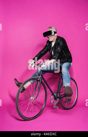 Smiling senior homme portant un casque de réalité virtuelle et équitation location isolé sur pink Banque D'Images