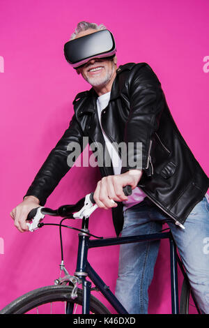 Hauts élégant homme portant un casque de réalité virtuelle et équitation location isolé sur pink Banque D'Images