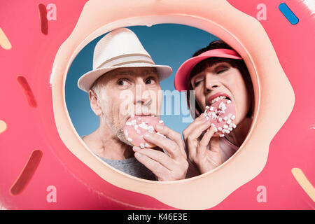 Portrait of elderly couple manger des beignets sucrés en tube de natation Banque D'Images