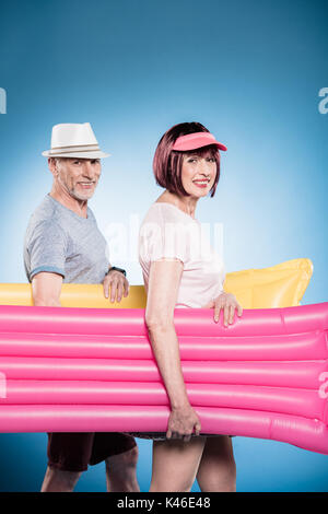 Happy senior couple looking at camera et la tenue de natation au cours de marche matelas Banque D'Images