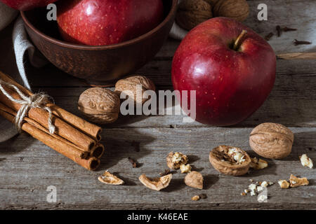 Des pommes rouges, des bâtons de cannelle et les noix sur la table rustique en bois Banque D'Images