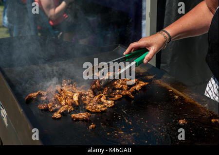 Faites cuire le poulet au barbecue sur une plaque chauffante en gros plan avec les mains du chef et les pinces pour hacher la viande Banque D'Images
