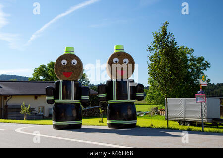 Deux modèles de pompiers faits de bottes de foin à l'extérieur de la station de pompiers en Esternberg & Augsburg, Haute Autriche, et Bavière, Allemagne. Banque D'Images