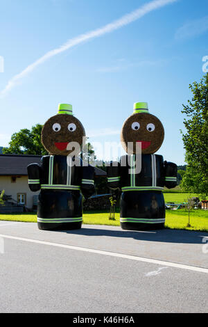 Deux modèles de pompiers faits de bottes de foin à l'extérieur de la station de pompiers en Esternberg & Augsburg, Haute Autriche, et Bavière, Allemagne. Banque D'Images