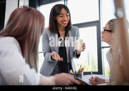 Smiling young businesswomen talking and drinking coffee in office Banque D'Images