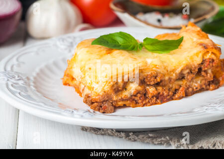 Close-up d'une lasagne traditionnelle faite avec du bœuf haché sauce bolognaise garnie de feuilles de basilic servi sur une plaque blanche Banque D'Images