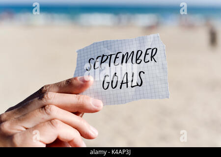 Libre de la main d'un jeune homme de race blanche tenant une note avec le texte écrit en objectifs septembre il, en face de la plage Banque D'Images