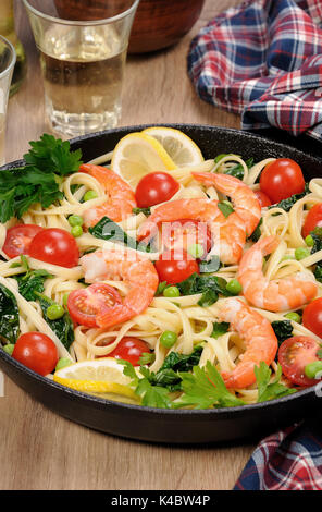 Pâtes aux crevettes frits, les pois, les tomates et les épinards dans une poêle, sur une table avec des verres de cidre. Banque D'Images