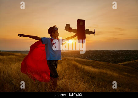 Un heureux garçon dans un costume de super-héro est de jouer avec un avion. Banque D'Images