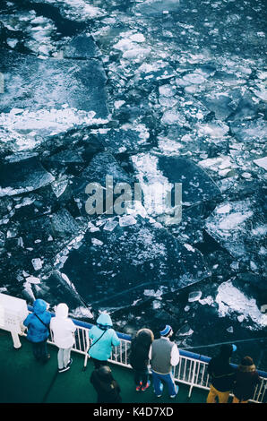 Des gens habillés en vêtements chauds se tenir sur le pont du navire et regarder des blocs de glace fissurée en mer en hiver Banque D'Images