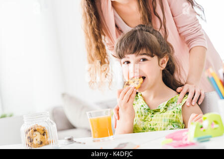 Cute girl d'âge préscolaire ayant une collation avec sa mère, elle est en train de manger des biscuits délicieux, la nutrition et le mode de vie concept Banque D'Images