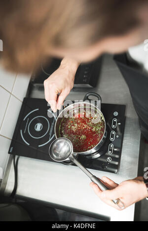 Portrait de dessus du chef cuisson de la soupe sur une plaque à induction L'ajout d'épices Banque D'Images