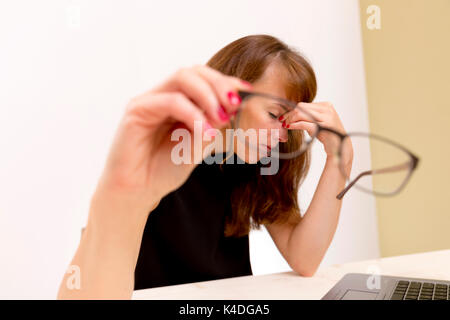 Se sentir fatigué et stressé. Jeune femme frustrée en gardant les yeux fermés et à masser le nez tout en restant assis à sa place de travail social Banque D'Images
