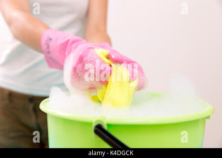 Close-up of woman hand squeezing chiffon dans seau rempli avec du savon Banque D'Images