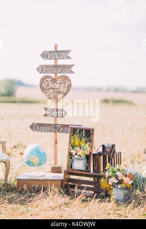 La photo verticale des plaques en bois avec les signes ''mariage, photo, dancing'' placé près de la boite en bois avec des fleurs, ancien appareil photo et d'un globe terrestre dans la zone ensoleillée. Banque D'Images