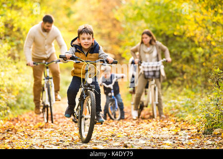 Jeune famille de vêtements chauds à vélo dans le parc en automne Banque D'Images