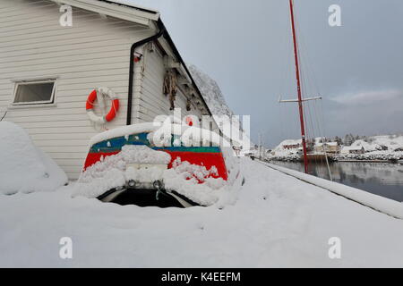 Les petits bateaux de pêche rouge-vert sous de fortes chutes de neige à terre aux côtés des entrepôts en bois blanc sur le pont-jetée du port de pêche, côté ouest-Festhaeltinden mont Banque D'Images