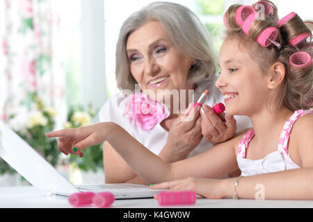 Cute little girl dans les bigoudis avec granny à l'aide d'ordinateur portable à la maison Banque D'Images