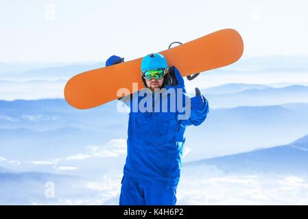 Happy man with snowboard à mains se dresse sur la vallée de montagne en toile de fond. planchiste ou snowboard concept Banque D'Images