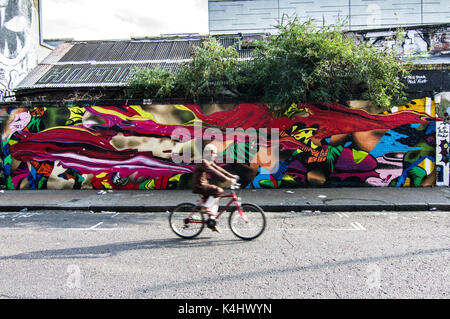 Musulman en brun, le visage brouillé depuis un vélo aux couleurs vives et éclatantes, fresque sur la rue sclater street près de Brick Lane, London, UK Banque D'Images