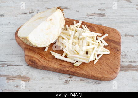 Céleri racine coupée en petits morceaux avec la moitié de l'ensemble de la racine de céleri sur une planche à découper en bois d'olivier sur un fond en bois clair. étape par étape faire cuire Banque D'Images