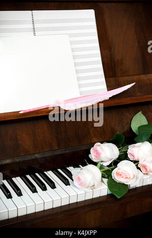 Piano, roses rose pâle sur le clavier, de musique et de papier vierge blanc avec plume rose. Banque D'Images