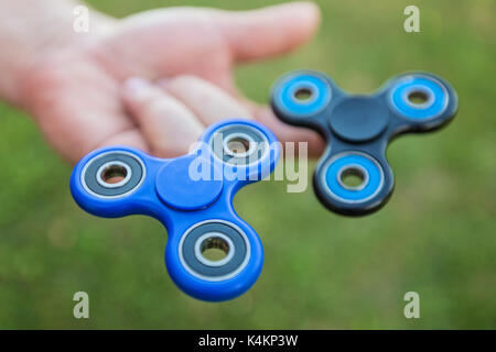 L'homme tenant deux fidget spinners sur ses doigts contre le fond d'herbe floue Banque D'Images