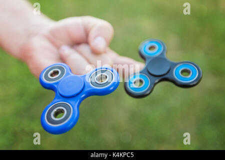 L'homme tenant deux fidget spinners sur ses doigts contre le fond d'herbe floue Banque D'Images