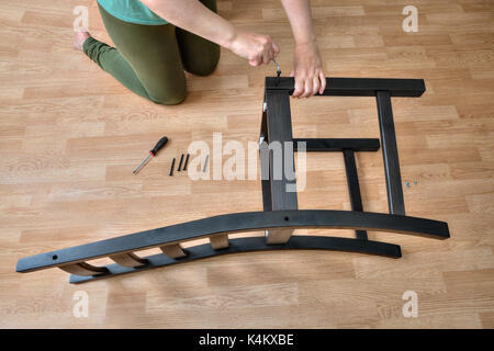 Assemblée des meubles en bois, une femme mettre ensemble les parties en bois de la chaise, à l'aide d'une clé six pans de la vis et de meubles. Banque D'Images
