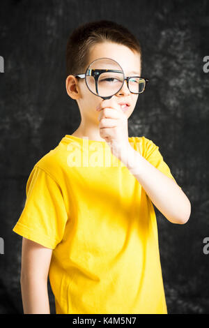 Garçon regardant à travers des lunettes et une loupe sur un fond sombre Banque D'Images