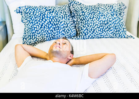 Jeune homme heureux portant sur le lit libre avec des oreillers, couette dans la chambre de house, maison ou appartement Banque D'Images