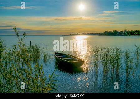 Bateau à rames sur le lac au coucher du soleil. petite barque en bois sur un lac calme au coucher du soleil. Banque D'Images