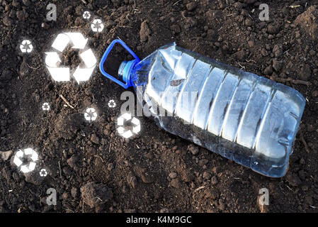 Pet 5 litres en plastique vide contenant potable tombé dans la terre brune avec recycler des signes épars sur le sol Banque D'Images