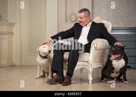 L'homme propriétaire de chien deux chiens de ferme. Black pit bull terrier ou staphorshire bulterrier blanc et sont dans l'intérieur d'époque. Les chiens assis de chaque côté Banque D'Images