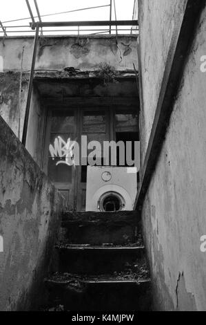 Escaliers de sous-sol et extérieur de maison abandonnée avec un lave-linge sur jour de pluie. Noir et blanc. Banque D'Images