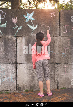 10 ans, petite fille, l'enseignement primaire l'âge, le dessin et l'écriture à la craie sur le béton. Banque D'Images