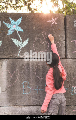 10 ans, petite fille, l'enseignement primaire l'âge, le dessin et l'écriture à la craie sur le béton. Banque D'Images