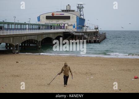 L'homme à l'aide d'un détecteur de métal sur la plage de Bournemouth avec la jetée de Bournemouth à l'arrière-plan Banque D'Images