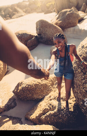 Jeune femme marchant à travers les rochers avec l'aide de son petit ami. Shot POV de man helping girlfriend climbing rock à la plage. Banque D'Images