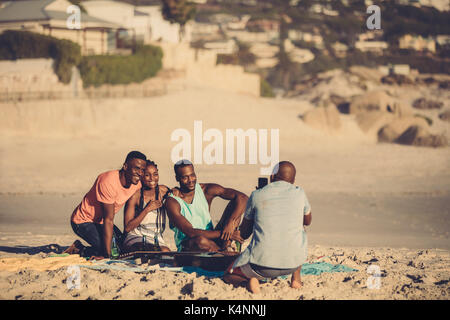 Jeune homme prend une photo de ses amis sur le bord de mer. Groupe d'amis sur la plage à prendre des photos. Banque D'Images