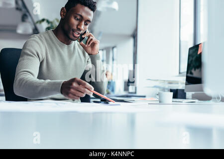 Businessman talking on smartphone et travaillant en bureau. African Male assis à son lieu de travail. Banque D'Images