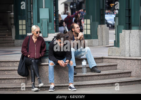 Londres, Angleterre - 20 août 2017 Deux hommes et une femme sont assis sur les marches près d'une station en attente d'amis Banque D'Images